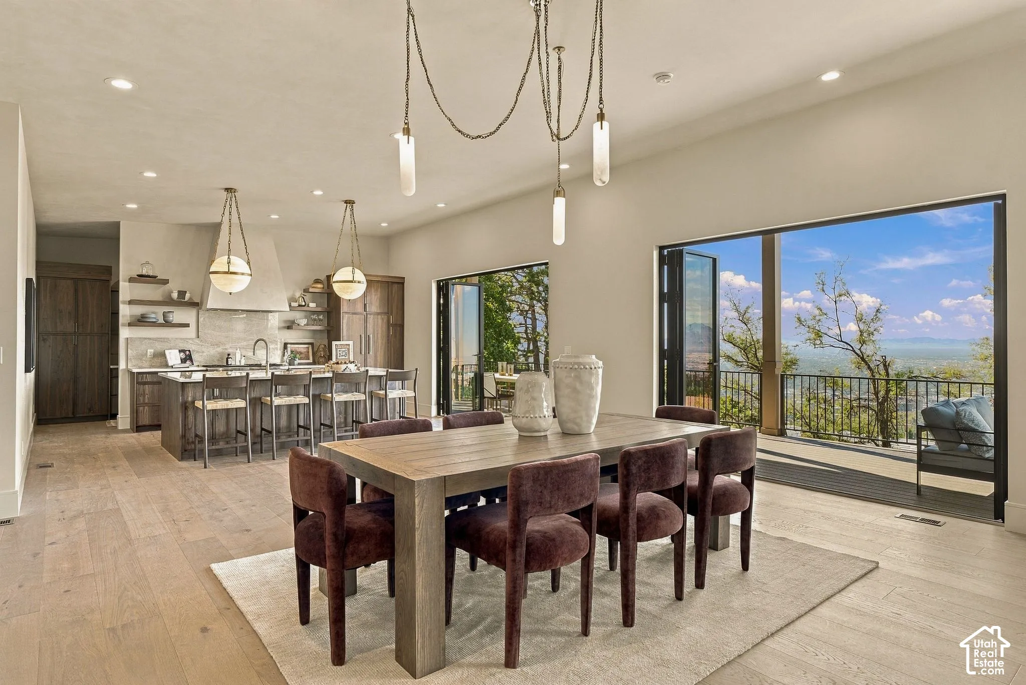 Open-concept interior featuring wood-finish flooring, multi-panel folding glass doors, custom kitchen cabinetry, a stone-surround range hood, and recessed lighting