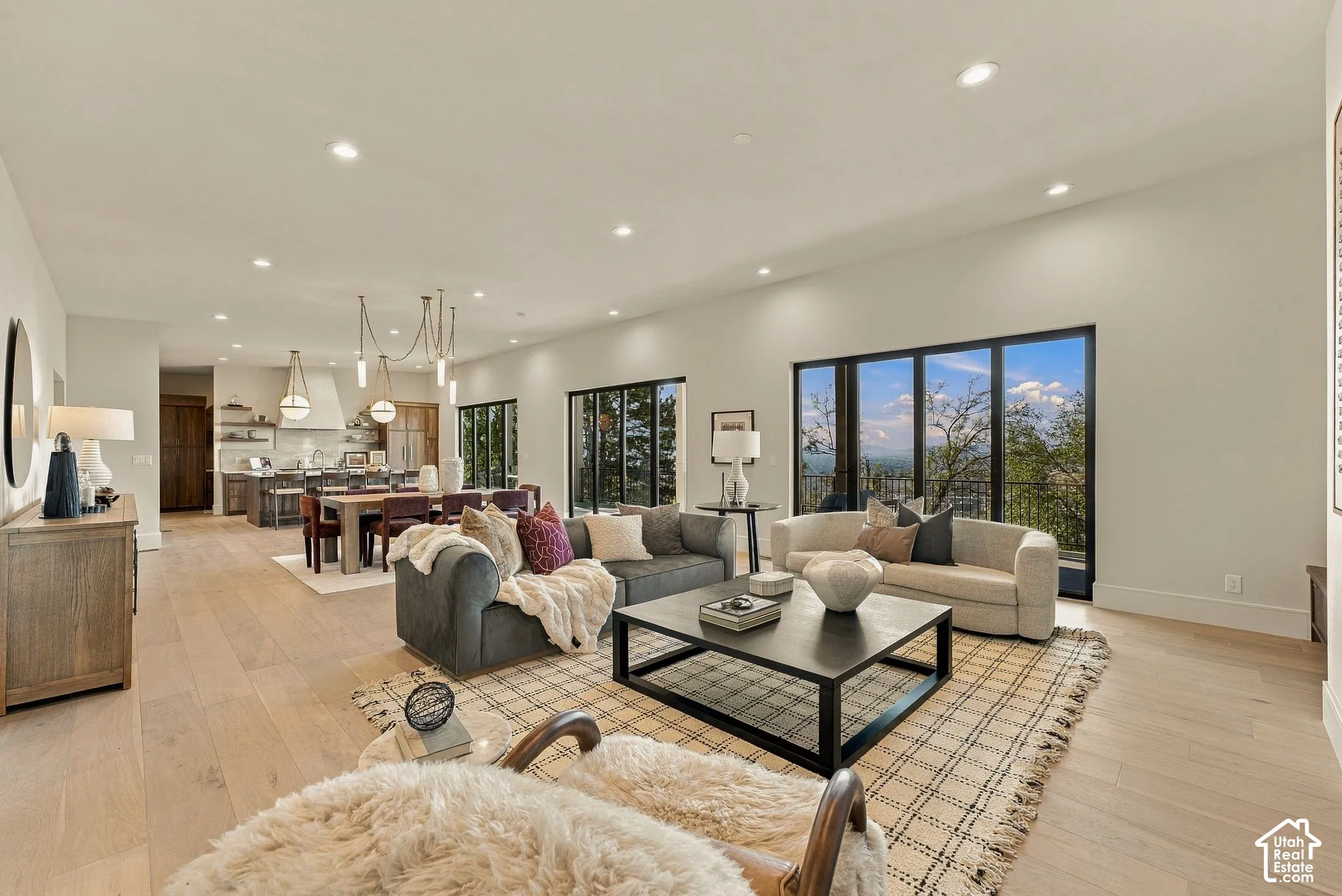 Open-concept interior featuring light wood-finish flooring, recessed lighting, expansive black-framed glass sliding doors, and a kitchen equipped with a large center island and modern pendant lighting