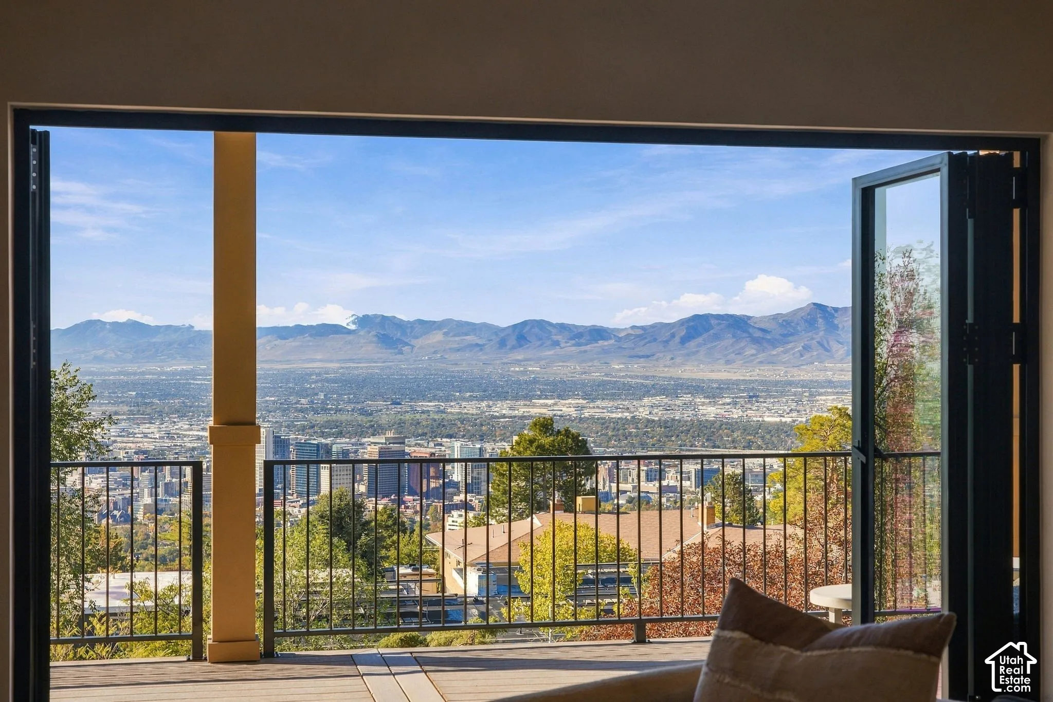 Floor-to-ceiling bi-fold glass doors, spacious exterior deck, metal railing, and panoramic mountain and city scenery