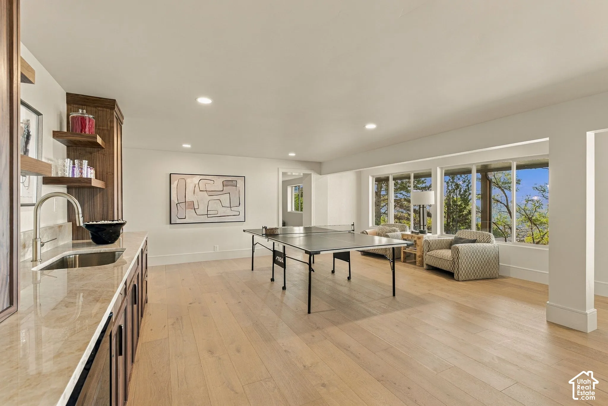 Wet bar featuring custom wood cabinetry, stone countertops, integrated sink, and tiered floating shelving, complemented by wide-plank wood-finish flooring and a expansive window array