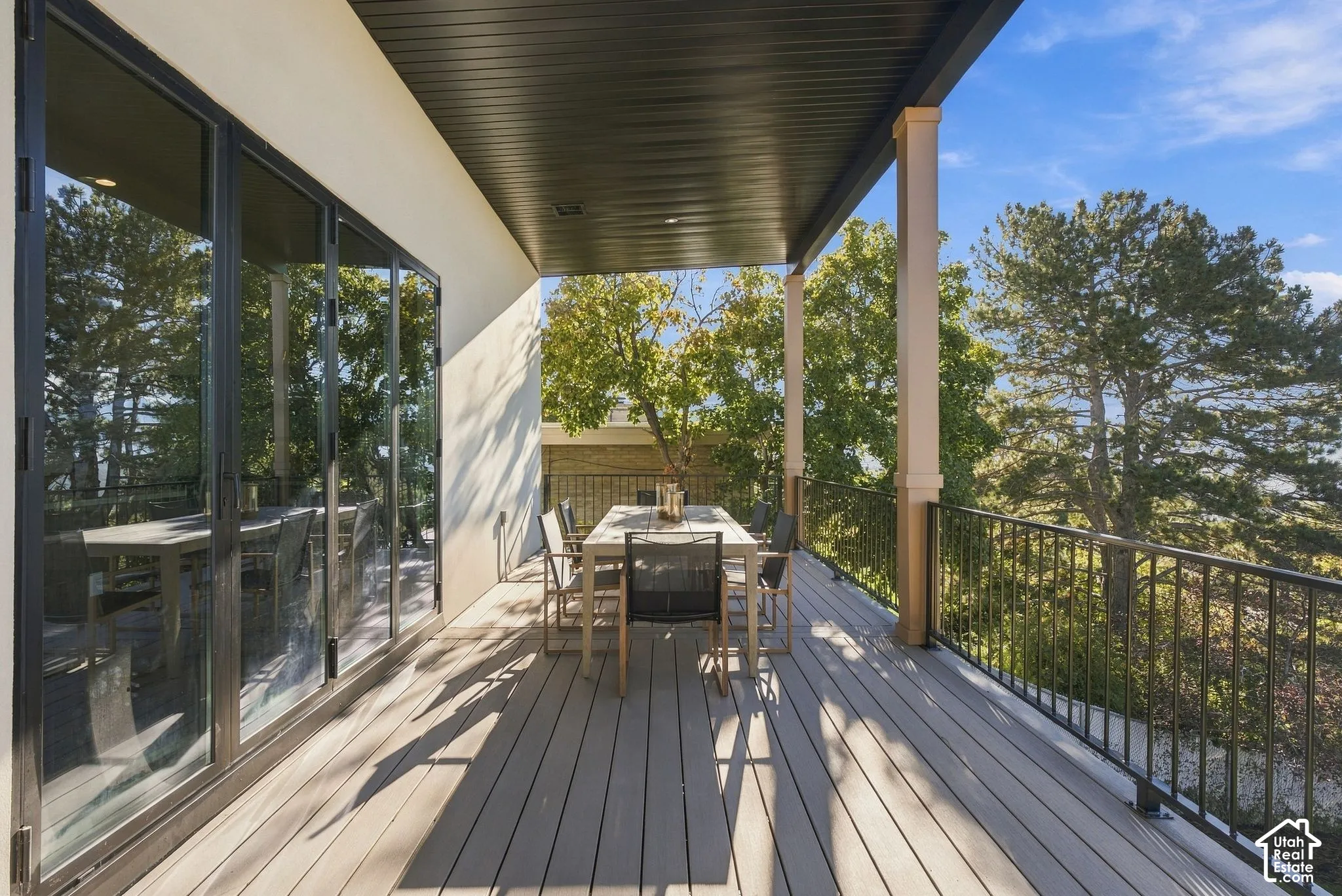 Covered deck featuring composite decking, black metal railings, floor-to-ceiling glass panel doors, and recessed lighting