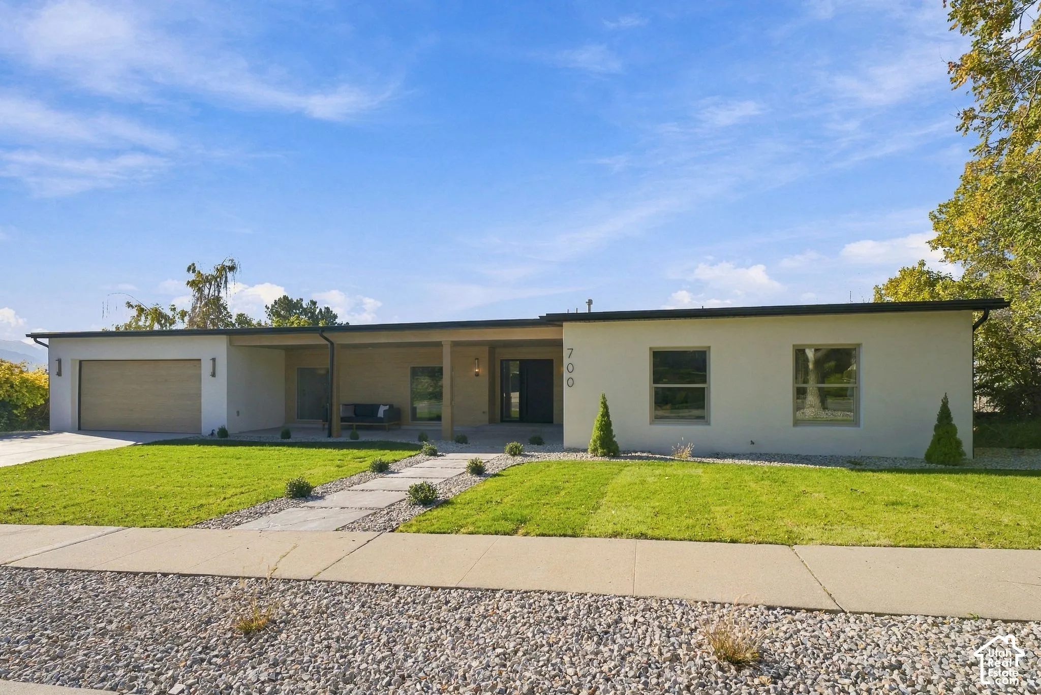 Single-story exterior featuring a smooth stucco finish, recessed covered entryway, integrated two-car garage, wood-texture garage door, and a stone paver walkway