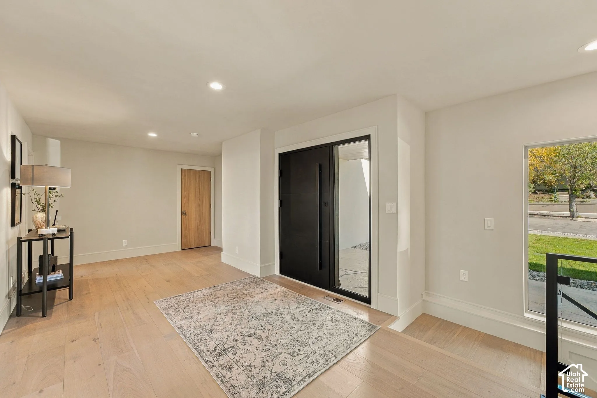 Entryway featuring wide-plank wood-finish flooring, a modern black paneled entry door with sidelight, recessed lighting, and large rectangular windows