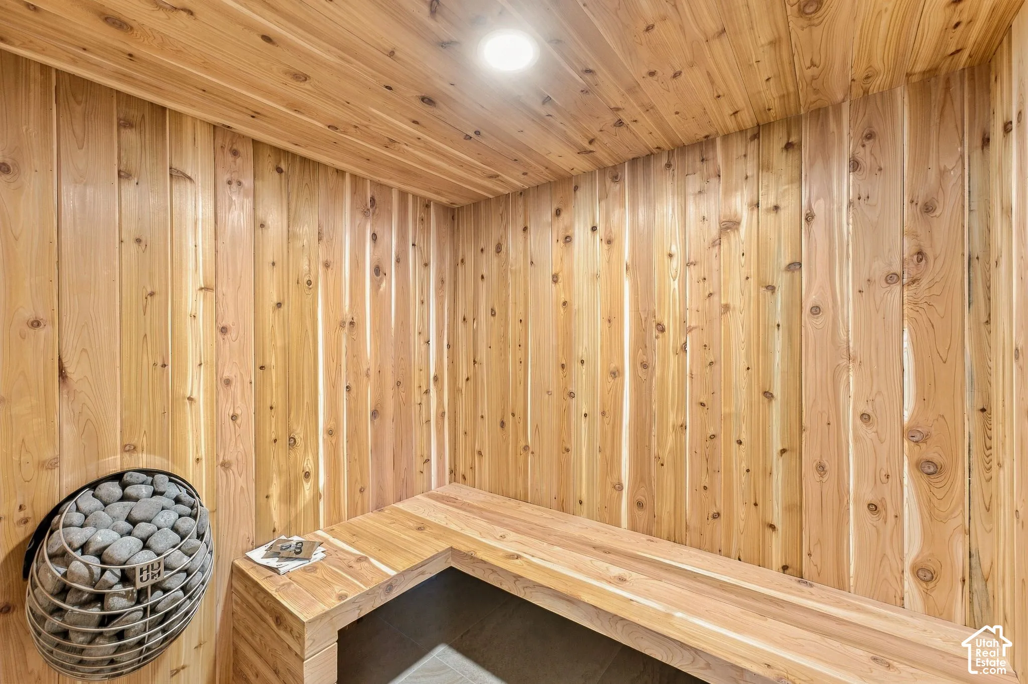 Sauna featuring tongue-and-groove wood paneling on the walls and ceiling, built-in wooden bench seating, and a wall-mounted metal heater with stones