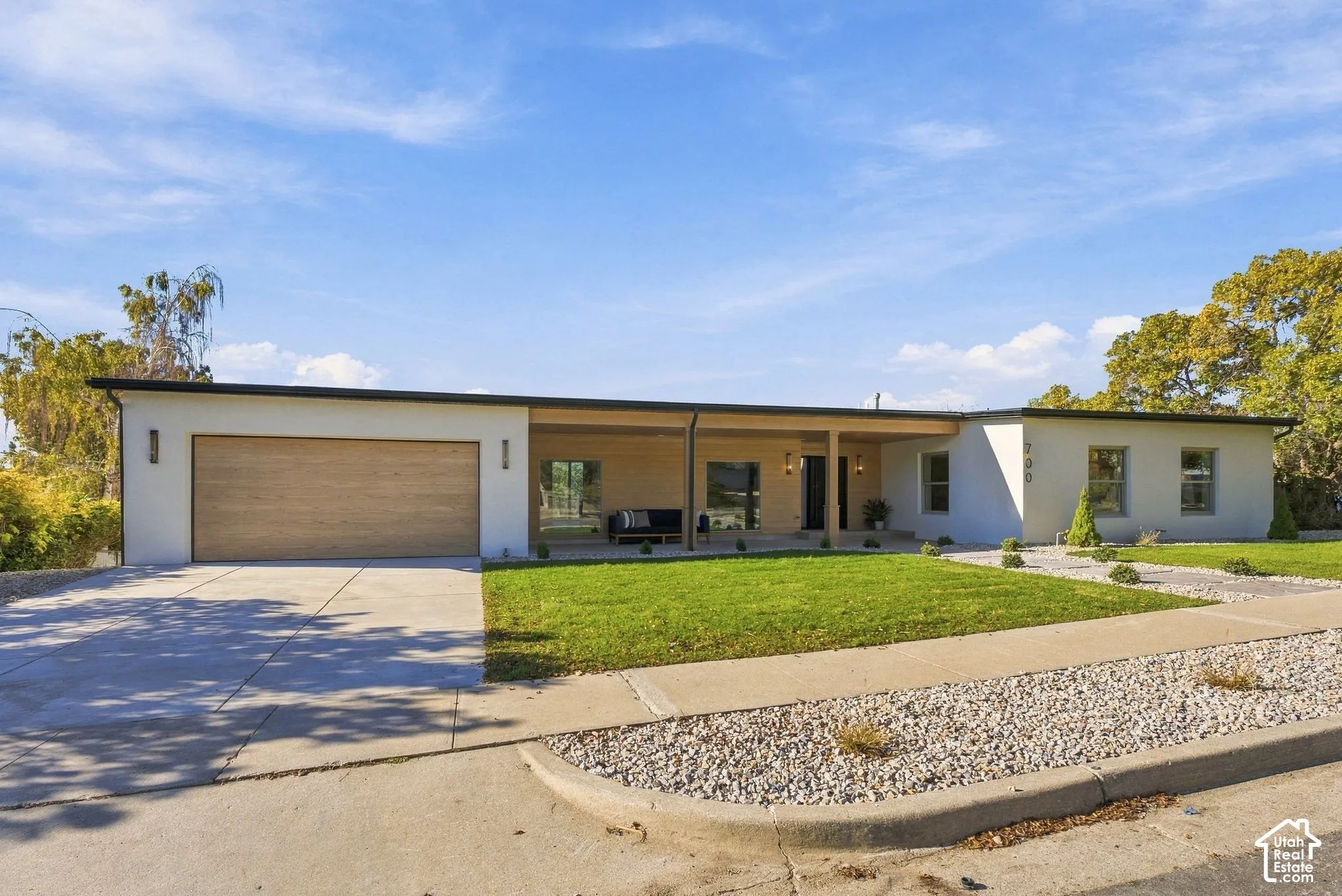 Mid-century modern residence featuring a smooth stucco facade, wood-finish garage door, covered porch with wood-plank ceiling, and xeriscaped front landscaping