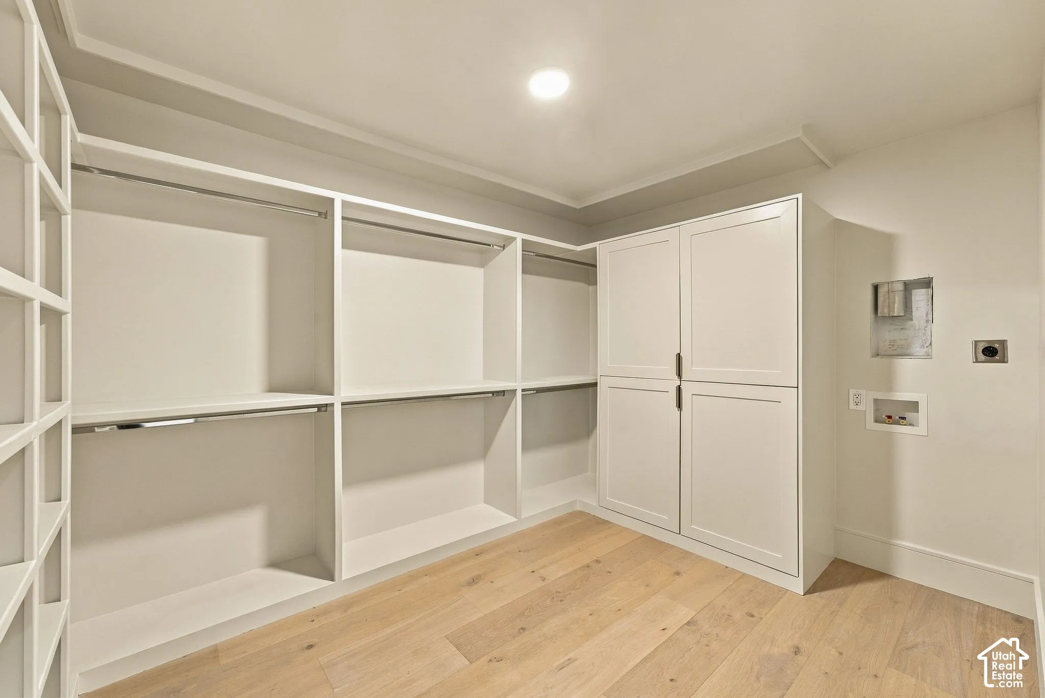 Custom walk-in closet featuring white built-in shelving, dual hanging rods, enclosed cabinet storage, and wood-finish flooring