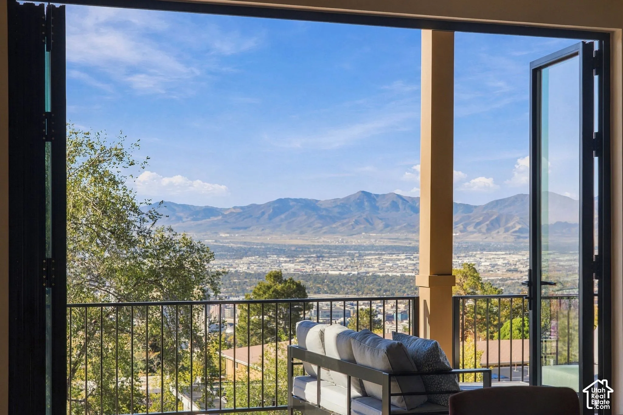 Floor-to-ceiling bi-fold glass doors, covered balcony, black metal railing, and mountain backdrop