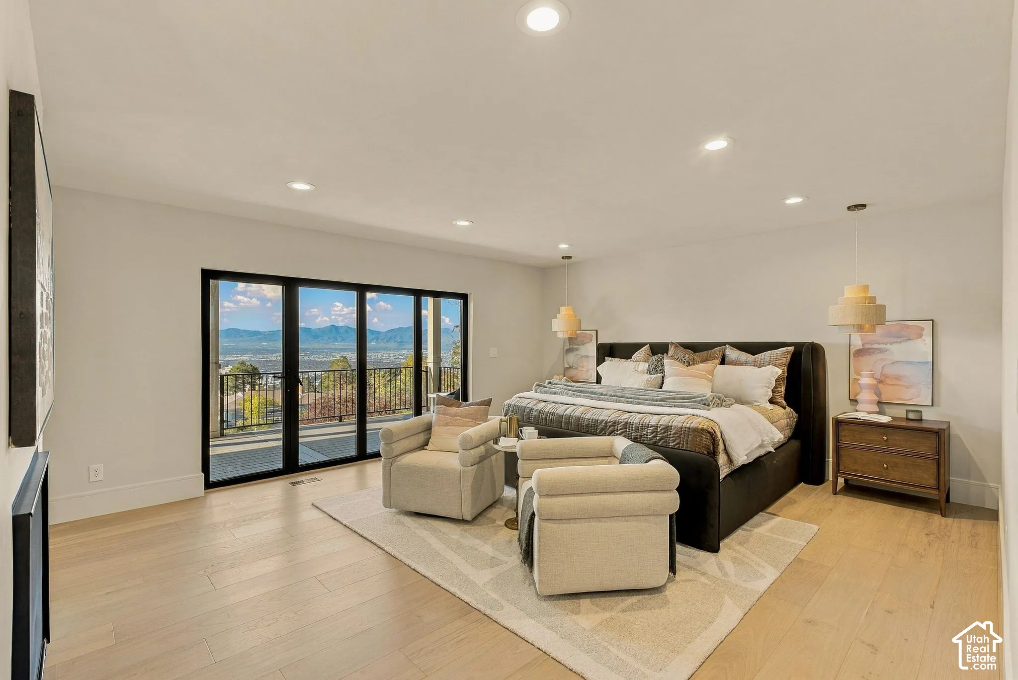 Floor-to-ceiling black-framed glass doors, wood-finish flooring, recessed lighting, dual pendant lights, and access to a balcony with mountain scenery