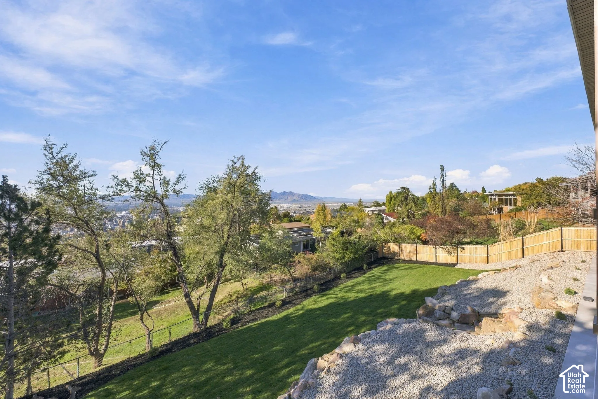 Multi-level backyard featuring a manicured lawn, tiered stone retaining walls, wood privacy fencing, and mountain scenery