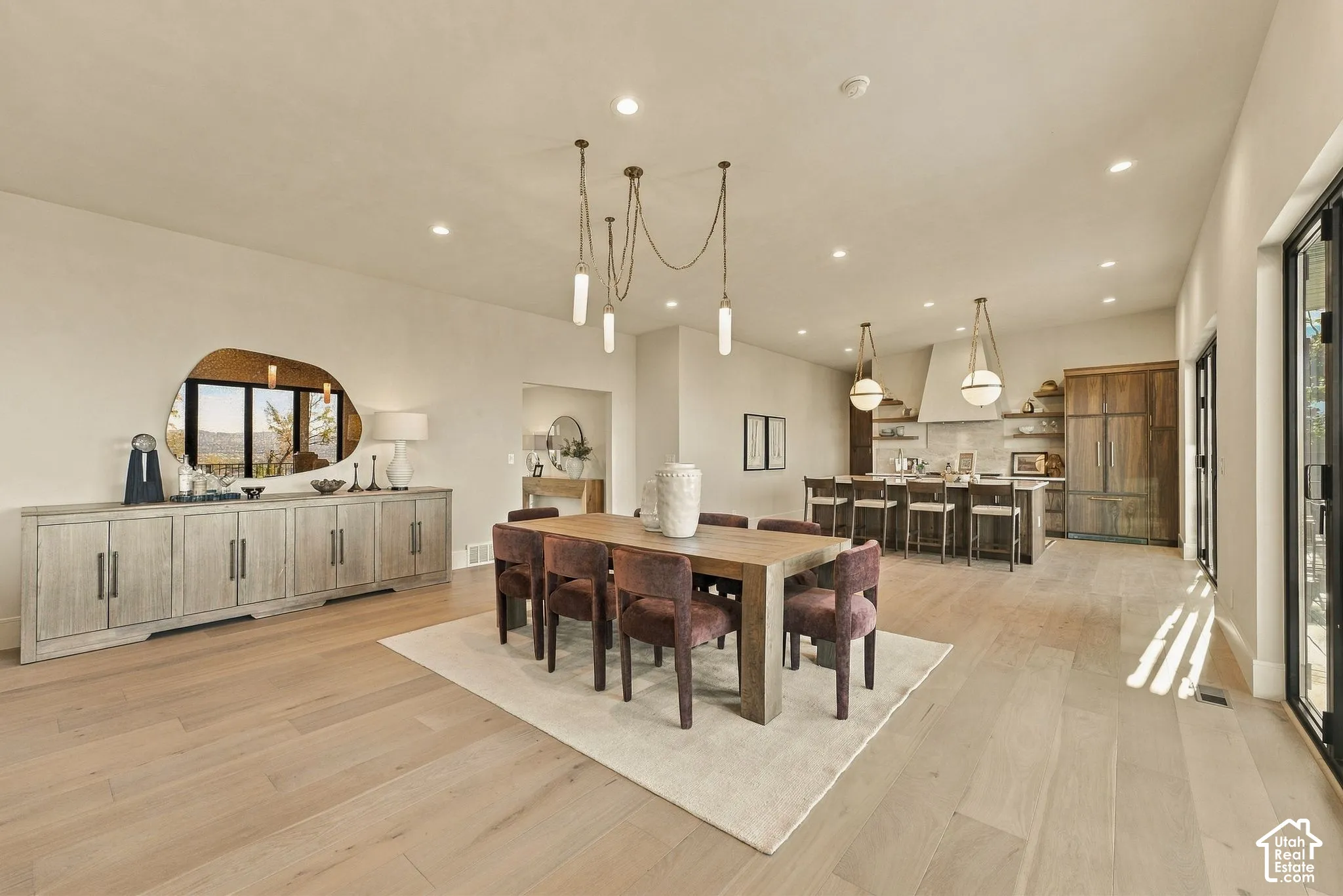 Open-concept interior featuring light wood-finish flooring, recessed lighting, built-in cabinetry with hardware, a center island with pendant lighting, and full-height wood-paneled integrated refrigeration