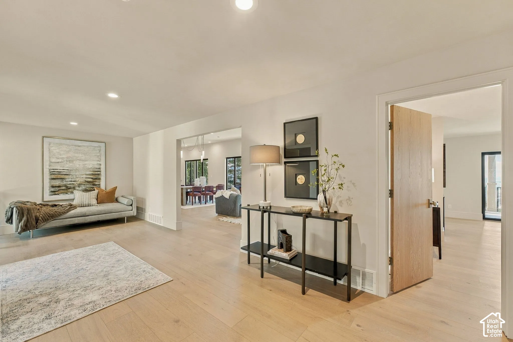 Open-concept interior featuring light wood-finish flooring, neutral wall paint, recessed lighting, and a solid-core wood door