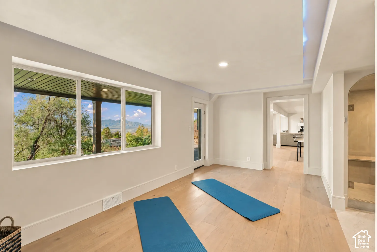 Large-format window featuring mountain scenery, recessed ceiling lighting with accent illumination, wood-finish flooring, and a glass-enclosed shower with an arched opening