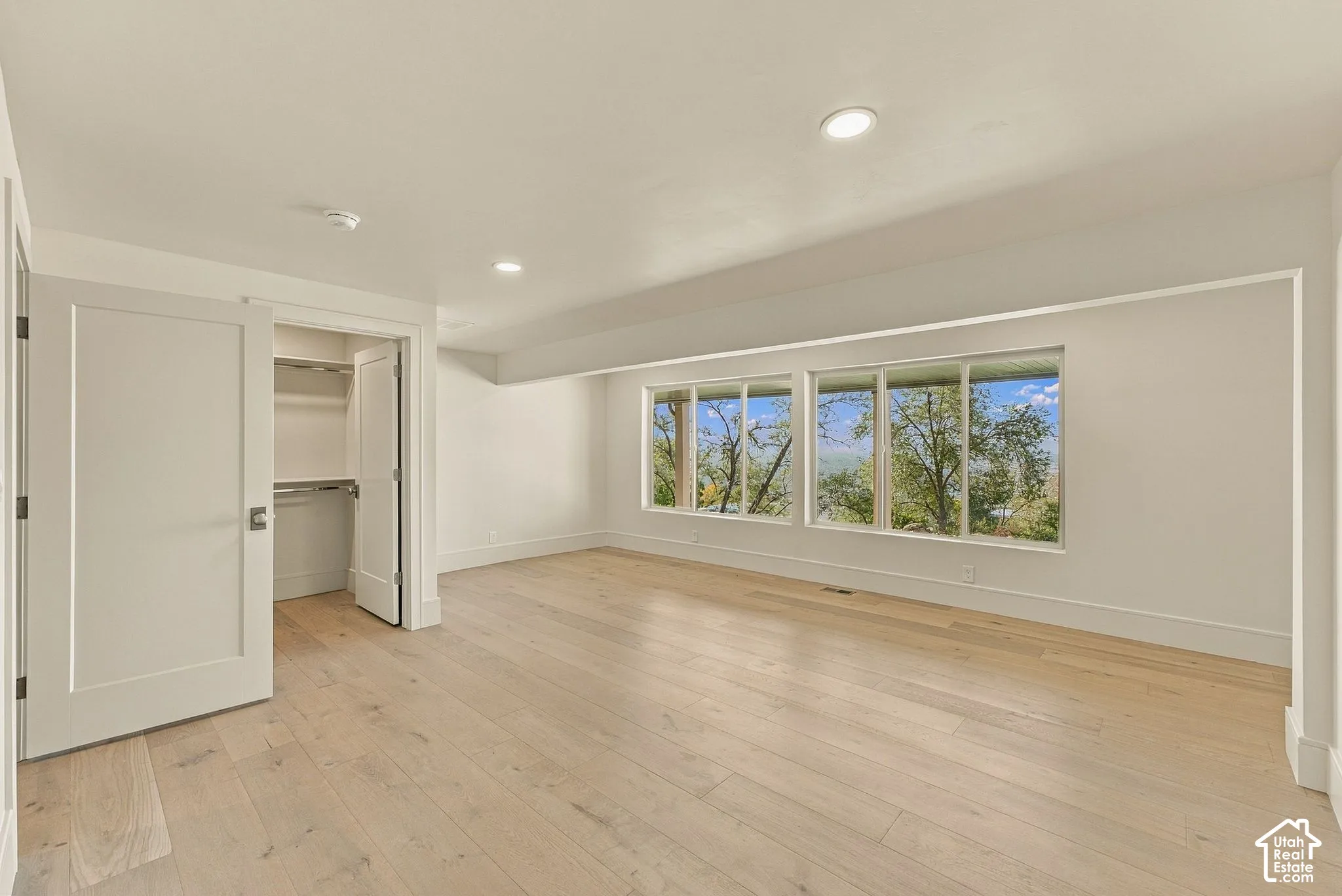 Interior space featuring wood-finish flooring, recessed lighting, expansive triple-pane window configuration, and an integrated walk-in closet with built-in shelving