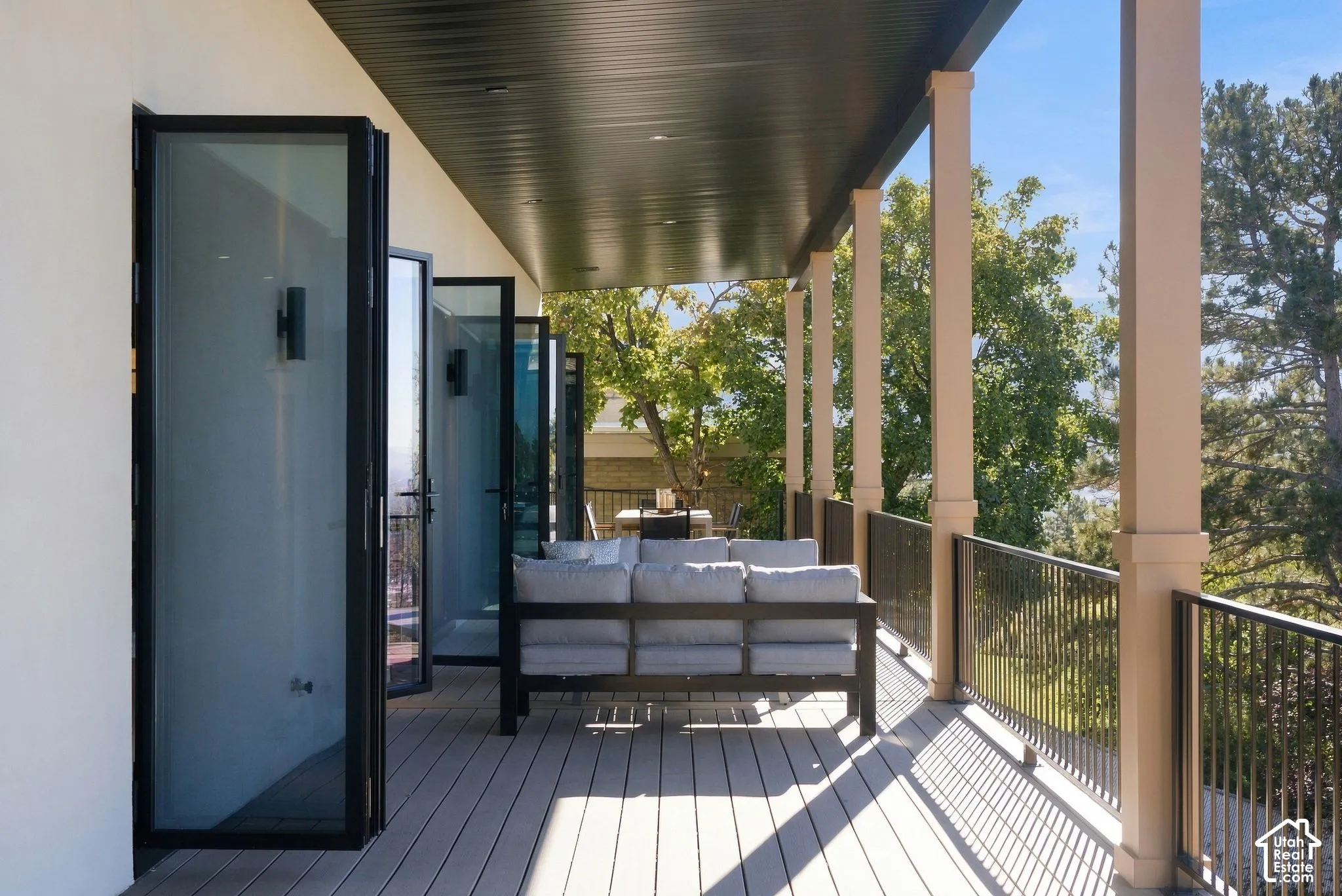 Covered balcony featuring multi-panel folding glass doors, composite decking, black metal railings, and recessed ceiling lighting