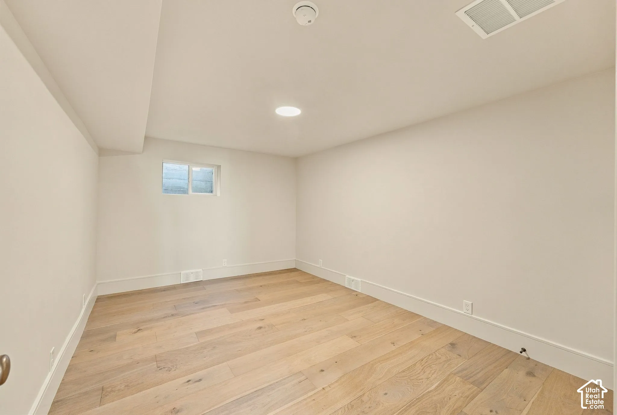 Neutral-toned interior space featuring light wood-finish flooring, recessed ceiling lighting, and a single-pane window
