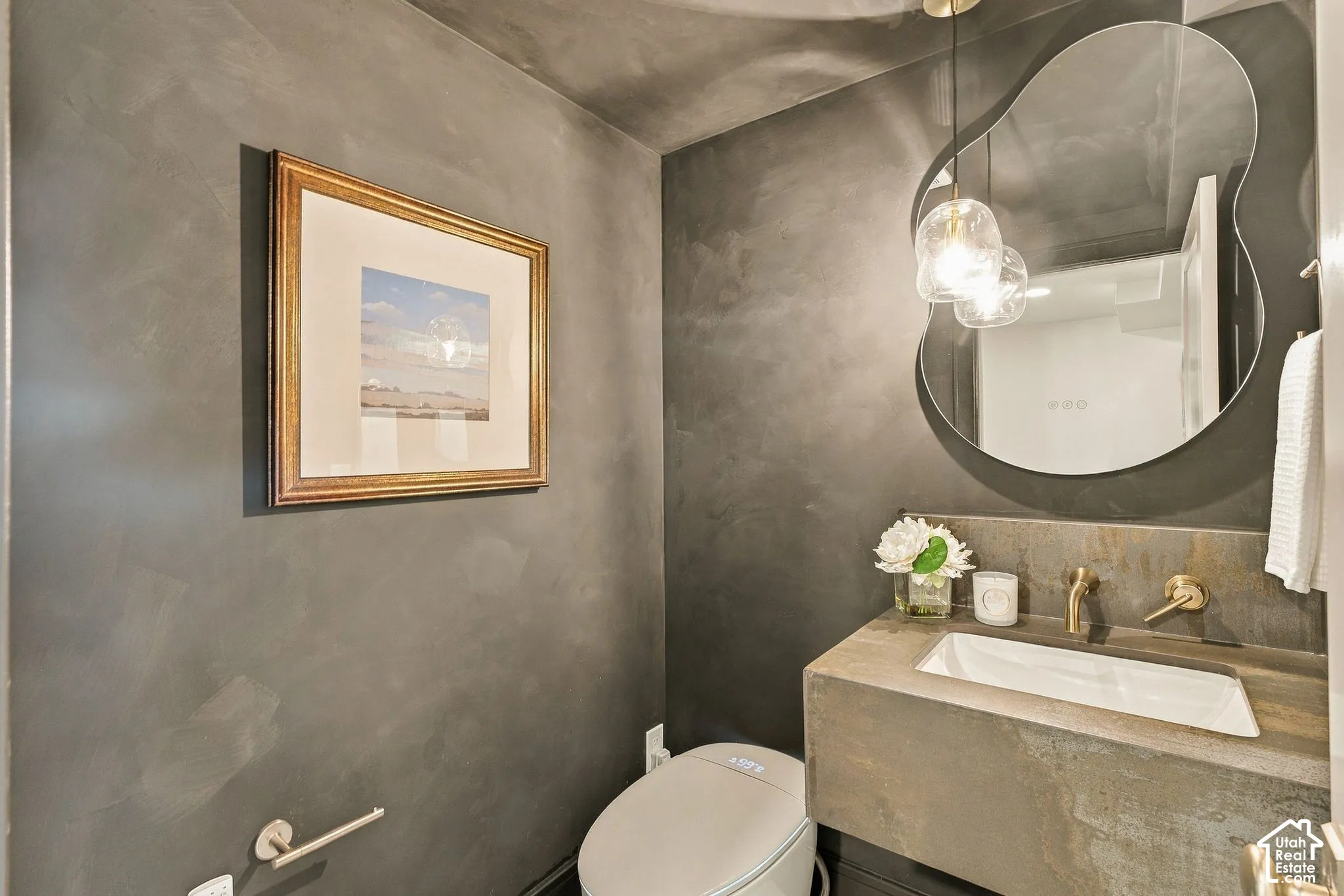 Textured charcoal walls paired with a custom stone floating vanity, integrated rectangular basin, matte gold-finish wall-mounted faucet, and an organic-shaped wall mirror with pendant lighting
