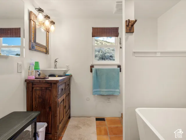 Bathroom vanity with dark wood-finish cabinetry, rectangular vessel sink, polished metal faucet, decorative wood-frame mirror with integrated lighting, and terra-cotta tile flooring