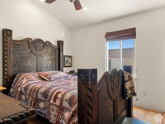 Vaulted ceiling featuring a central ceiling fan and neutral wall finish, complemented by stone-tile flooring and a window with a built-in shutter