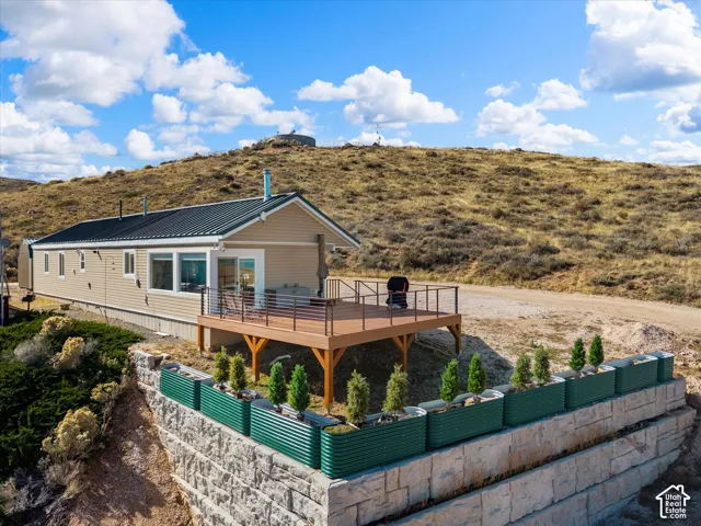Exterior featuring a raised composite deck with cable railings, a metal roof, and stone-block retaining walls with integrated steel garden planters