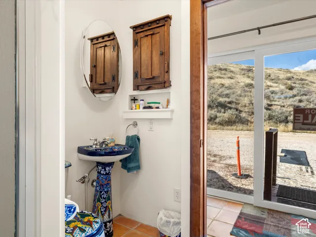 Custom-patterned pedestal sink, oval wall-mounted mirror, built-in wooden cabinet, and terra cotta floor tiles