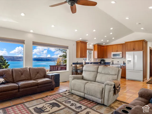 Open-concept area featuring vaulted ceilings, recessed lighting, tile flooring, and wood-finish cabinetry, with large windows overlooking a lake and mountain backdrop