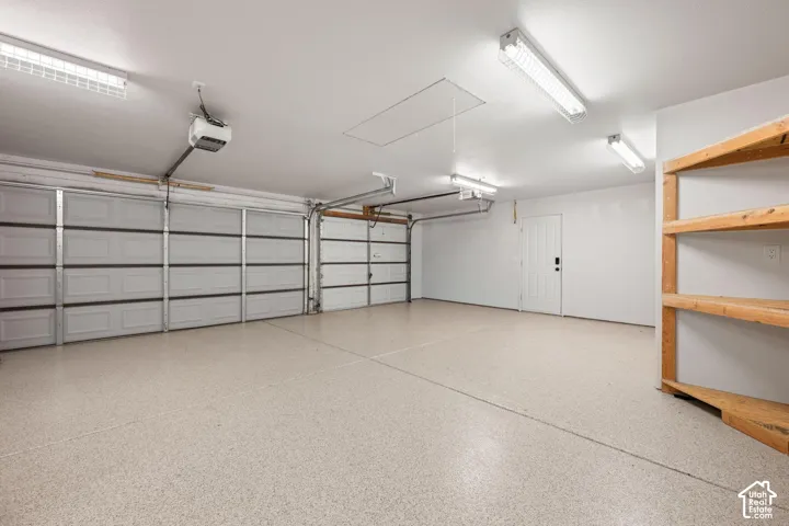 Multi-car garage featuring a speckled epoxy floor coating, white panel doors, built-in wooden shelving, and high-output linear fluorescent lighting