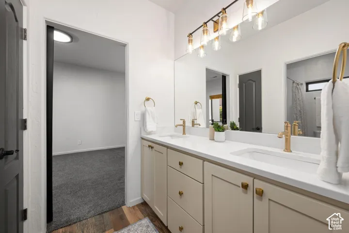 Double vanity with white solid-surface countertop, gold-toned hardware, undermount sinks, and a five-bulb linear vanity light fixture