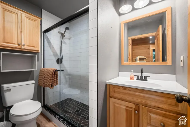 Bathroom featuring a vanity with wood-finish cabinetry, a white countertop, and a framed mirror, alongside a walk-in shower with white subway tile walls, a matte black rainfall showerhead, and dark hexagonal floor tiles