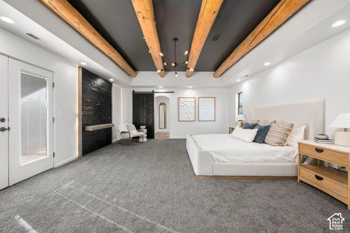 Vaulted ceiling featuring exposed timber beams, dark-toned accent wall with integrated shelf, black sliding barn door, recessed lighting, and glass-paneled exterior door