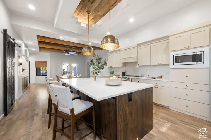 Kitchen featuring an oversized central island with wood-finish cabinetry, stone-surface countertop, ceiling beams, recessed lighting, and dual metallic pendant fixtures