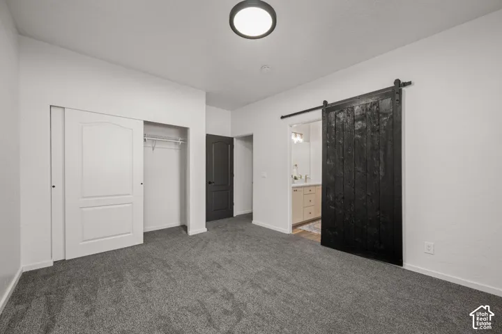 Interior space featuring grey carpeting, a black sliding barn door, a white sliding-panel closet door, a solid-core dark-finish interior door, and a flush-mount circular ceiling light