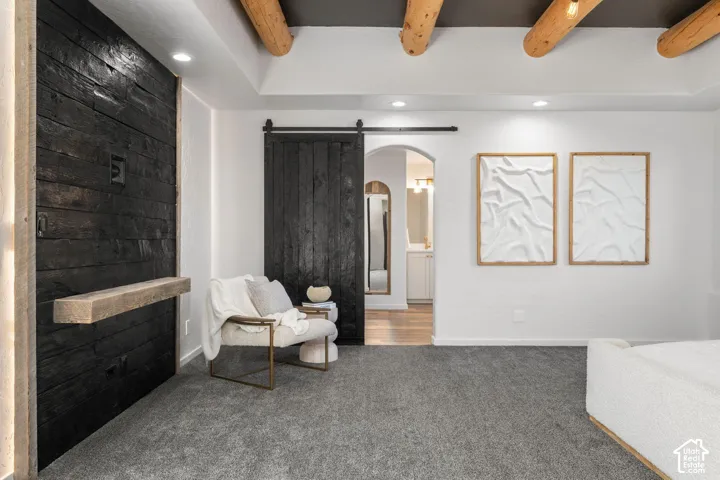 Exposed timber ceiling beams, black shiplap accent wall with a floating wood mantel, black sliding barn door, and arched doorway