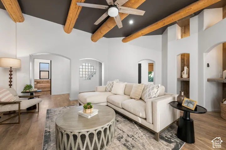 Vaulted ceiling with exposed log beams, wood-finish flooring, recessed built-in shelving, glass block accent window, and arched doorways