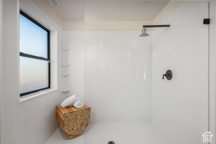 Walk-in shower with floor-to-ceiling white subway tile, frameless glass enclosure, rain-style showerhead, wall-mounted handle, and integrated corner shelving
