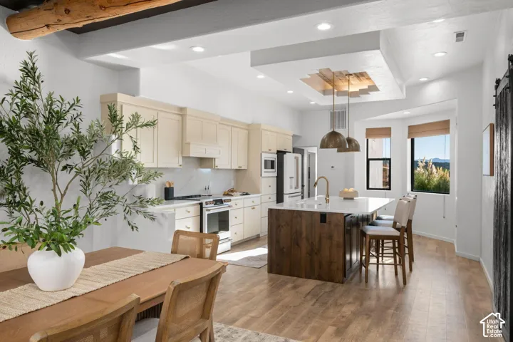 Kitchen featuring an island with a wood-finish base and light-toned solid surface countertop, light-toned cabinetry, recessed lighting, wood-finish flooring, and recessed ceiling detail with wood accents