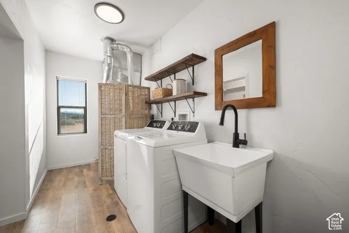 Utility room featuring wood-finish flooring, a utility sink with a matte black faucet, wall-mounted wood shelving, and a flush-mount overhead light fixture