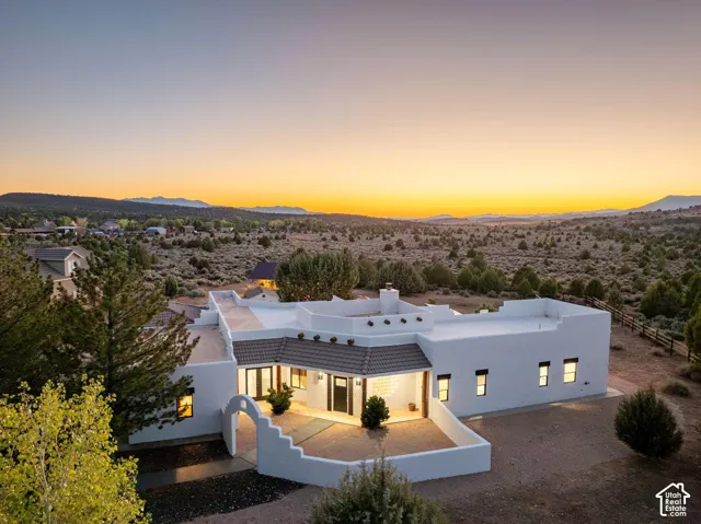 Pueblo-style exterior featuring a white stucco facade, parapet roofline with protruding vigas, arched courtyard entry, and a mountain backdrop