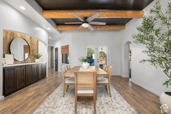 Dining area featuring exposed timber ceiling beams, a dark-toned flat-panel ceiling, wood-finish flooring, and built-in cabinetry with a wood-plank accent wall