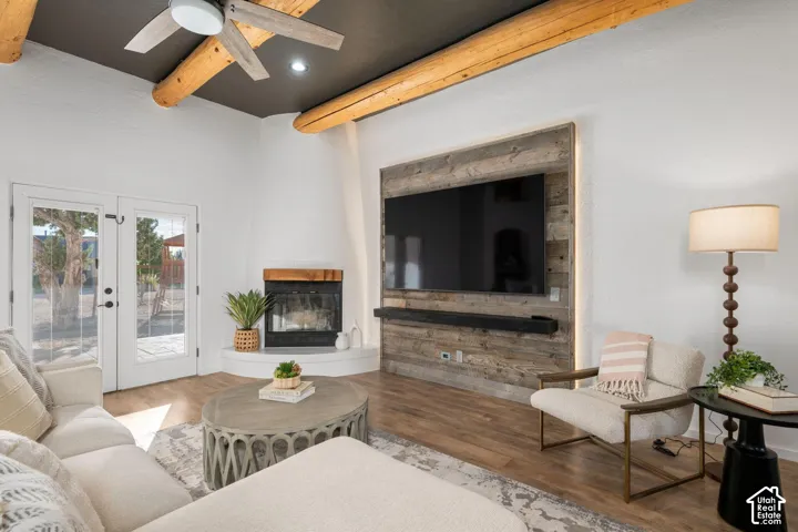Living area featuring exposed log ceiling beams, wood-finish flooring, corner fireplace with a stone mantel, reclaimed wood accent wall, and double glass-paneled exterior doors
