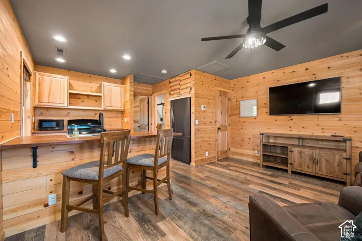 Natural wood paneling, wood-finish flooring, built-in kitchenette with a breakfast bar, recessed lighting, and a ceiling fan with integrated lighting
