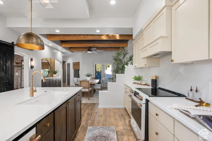 Kitchen featuring an expansive island with a light-toned countertop, custom cabinetry, exposed wood ceiling beams, wood-finish flooring, and a metal pendant light fixture