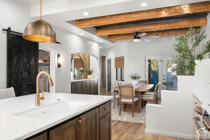 Exposed log ceiling beams, kitchen island with a light-tone solid surface countertop, brass-finish faucet, dark stained cabinetry, and a sliding barn door