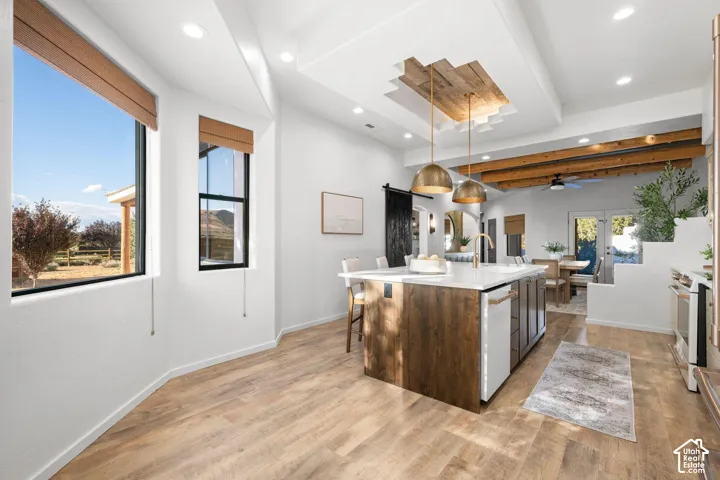 Kitchen featuring a central island with wood-finish cabinetry, quartz countertops, recessed ceiling detailing with wood-paneled inlay, exposed structural timber beams, and wood-finish flooring