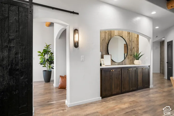 Built-in cabinetry with dark wood finish, vertical wood-plank wall accent, recessed wall arch, black sliding barn door, and wood-finish flooring