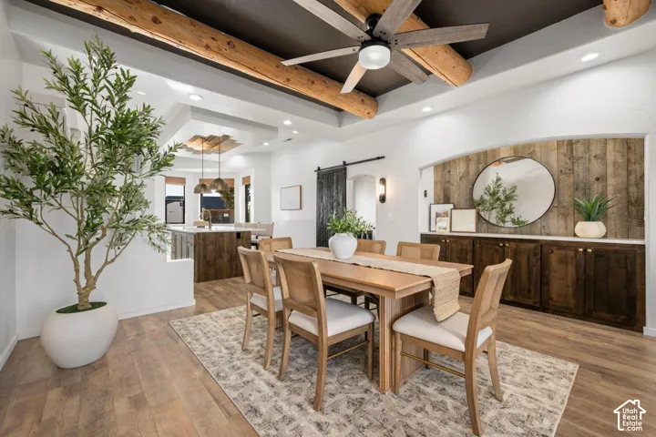 Open-concept dining and kitchen area featuring a wood-finish dining table with upholstered chairs, exposed ceiling beams, recessed lighting, and a large round mirror mounted on shiplap-style cabinetry