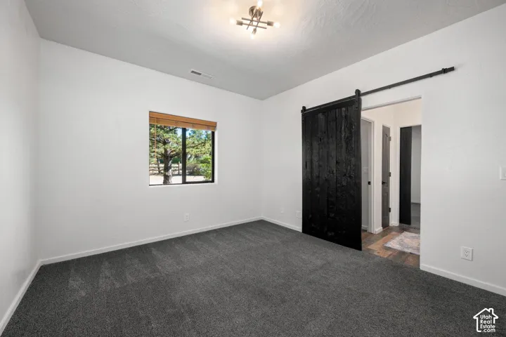 Room featuring charcoal carpeting, black sliding barn door, multi-bulb industrial-style ceiling fixture, and large window with wood-finish horizontal blinds