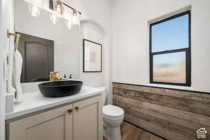 Bathroom featuring a vanity with a white countertop and black vessel sink, gold-tone faucet, wood-plank wainscoting, and a multi-light fixture