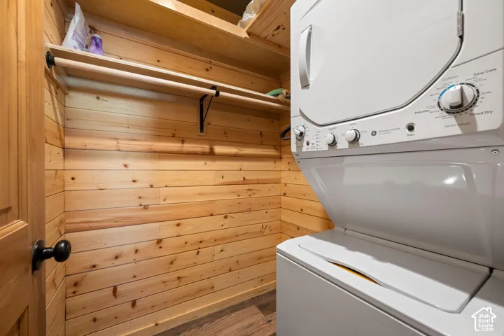 Natural wood plank wall paneling, built-in wooden shelving, integrated clothing rod, and stacked laundry unit