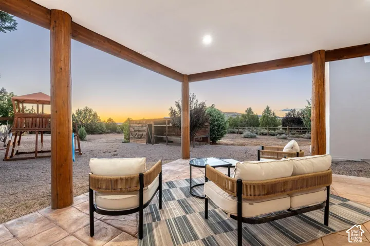 Covered patio featuring structural log support columns and tiled flooring, opening onto a gravel-surfaced yard with perimeter wood fencing