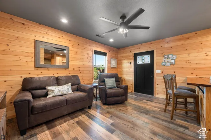 Horizontal wood wall paneling, wood-finish flooring, matte black ceiling fan with integrated lighting, recessed lighting, and a black entry door with a decorative glass insert
